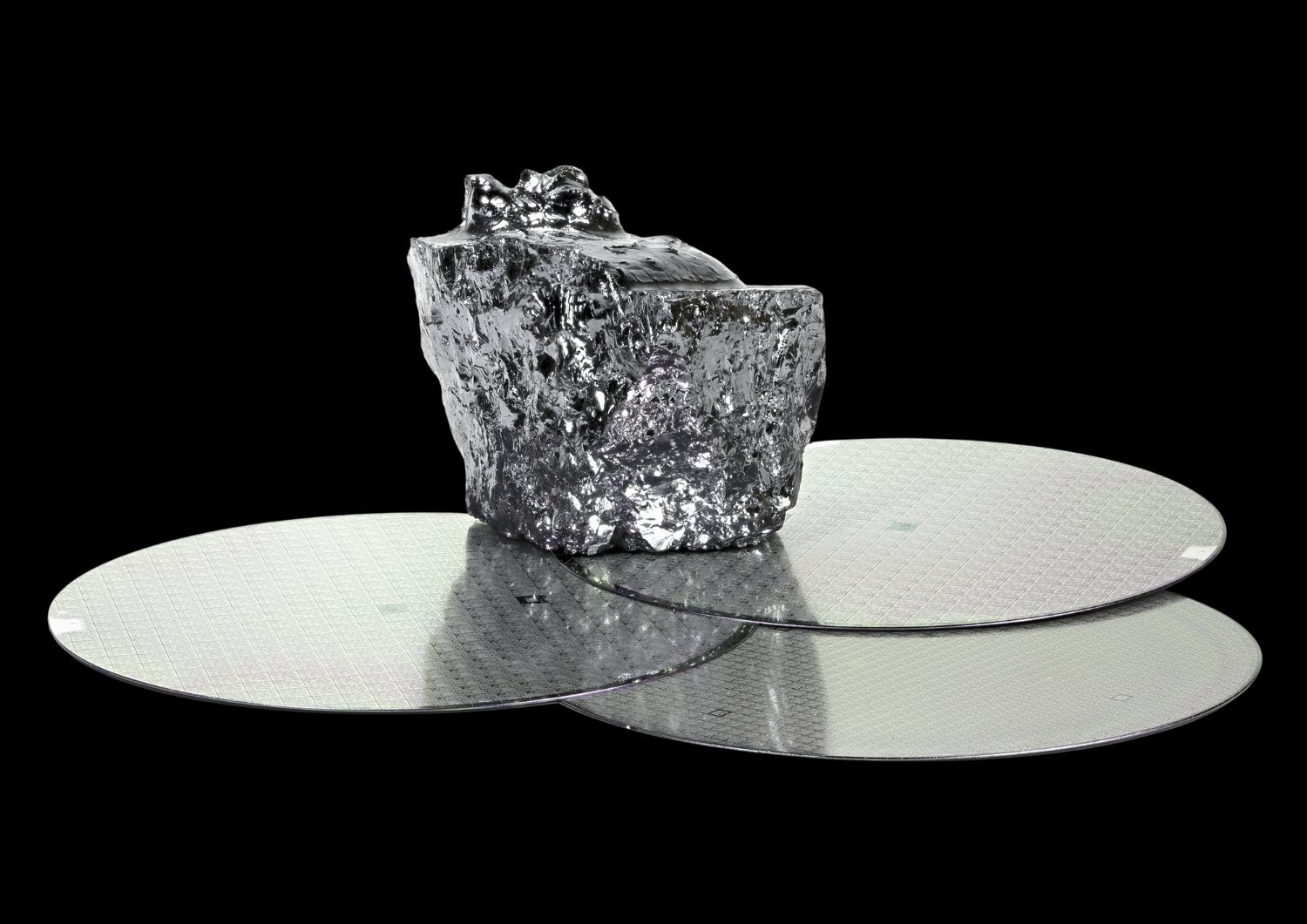 A hand holding a thin, reflective silicon wafer.